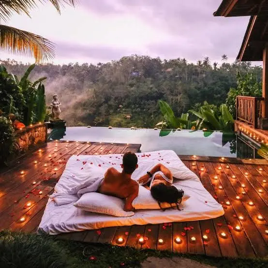 Couple relaxing on a candlelit bed beside an infinity pool at a tropical villa