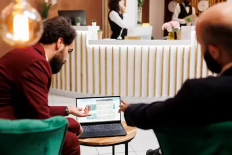 Dos personas revisan una plataforma en una notebook frente a la recepción de un hotel