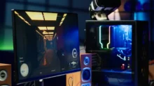 Monitor con videojuego en primera persona junto a una PC gamer iluminada y un visor de realidad virtual