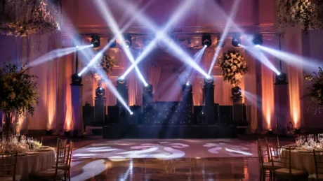 Salón de eventos con pista de baile, cabezales móviles y haces de luz sobre un escenario