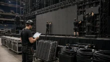 Crew members assembling a modular LED wall beside organized flight cases and cable bins in an arena.